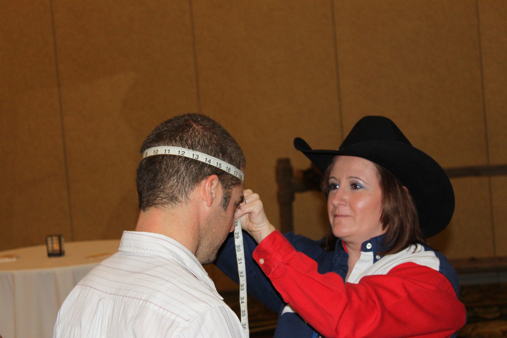 A woman measuring the head of a man wearing a cowboy hat.