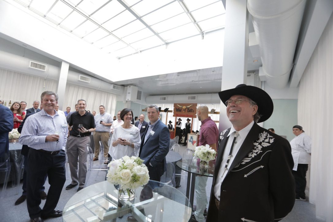 A man in a cowboy hat and suit stands next to a table.