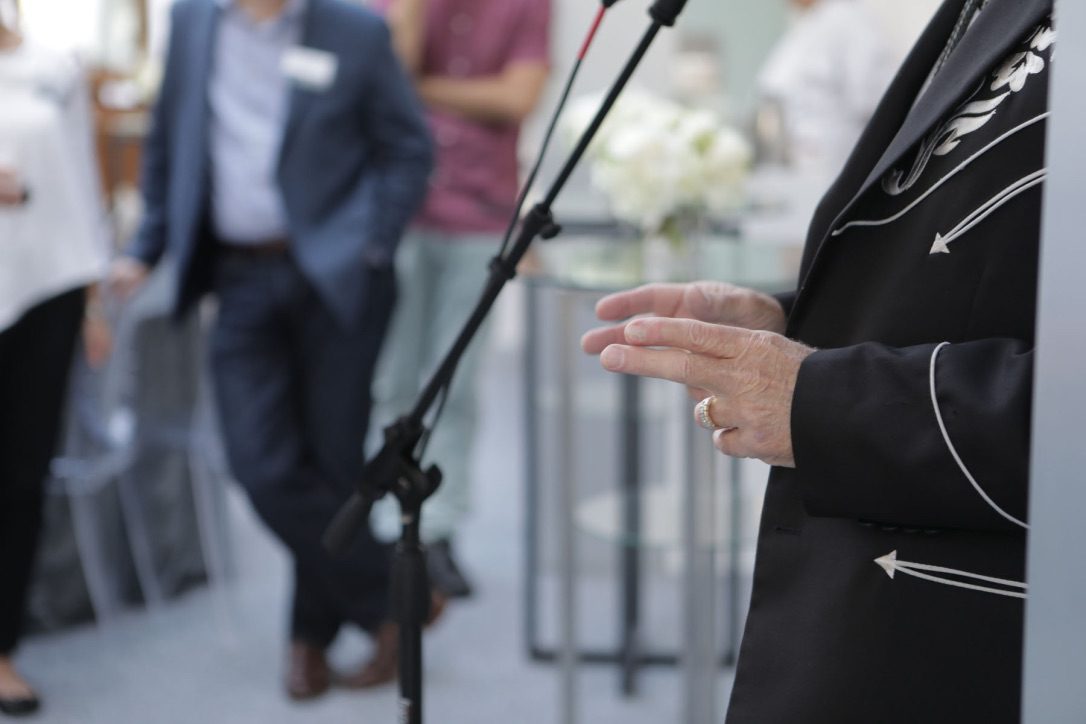 A person standing in front of microphones and other people.