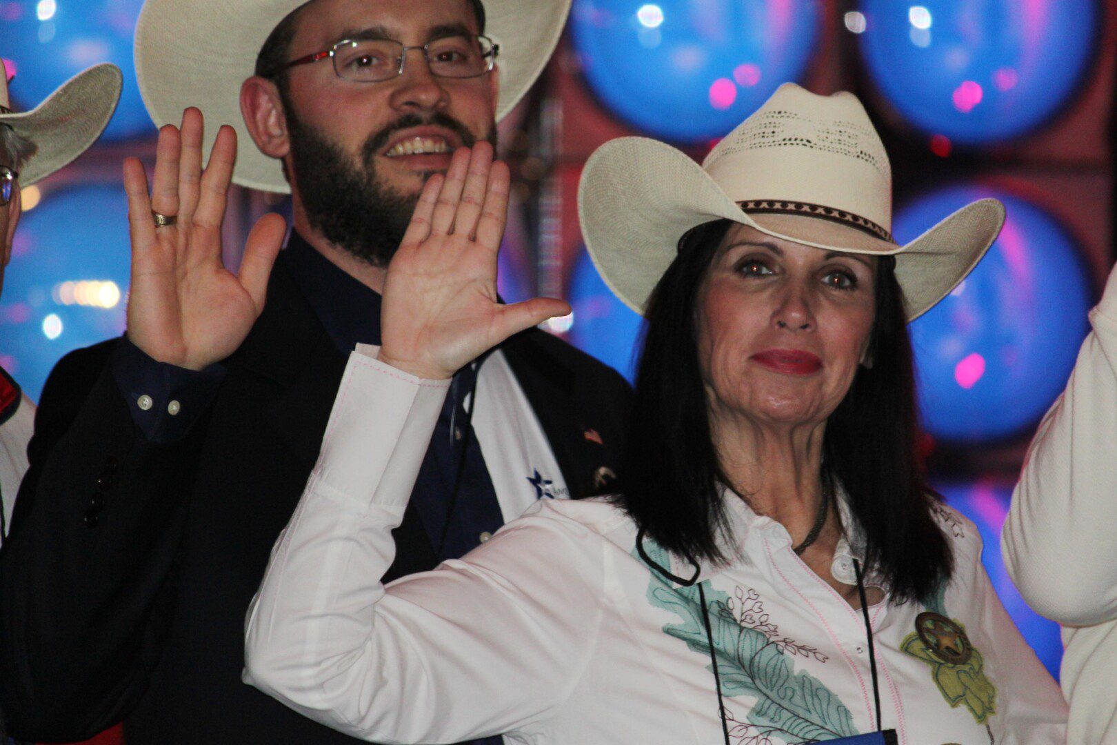 A man and woman in cowboy hats wave at the camera.