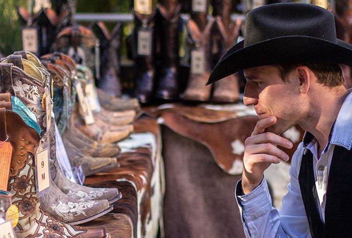 A man in cowboy hat looking at boots.