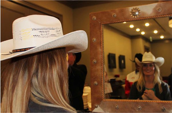 A woman in cowboy hat looking at her reflection in the mirror.