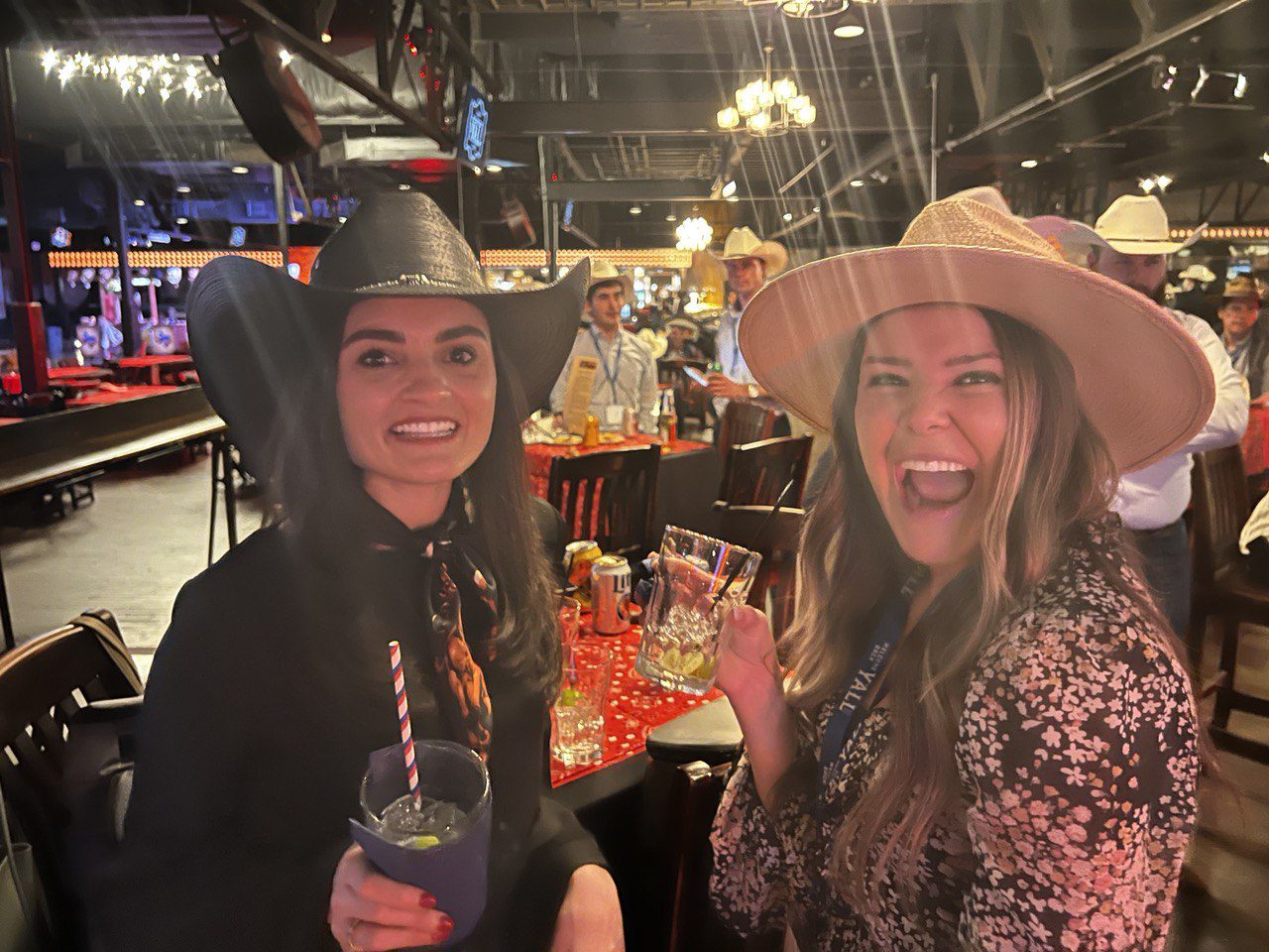 Two women wearing hats and holding drinks at a party.