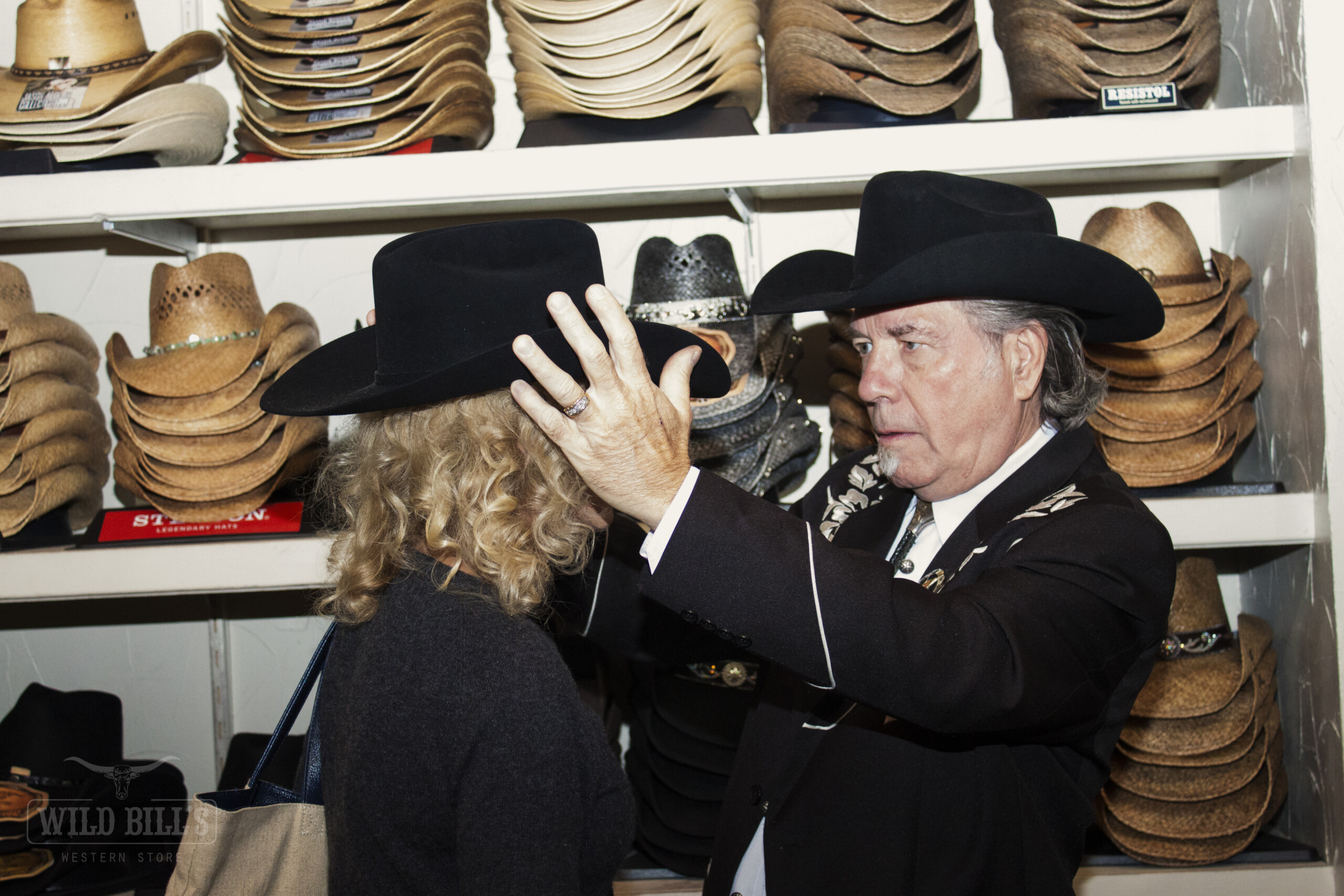 A man and woman in cowboy hats touching their heads.
