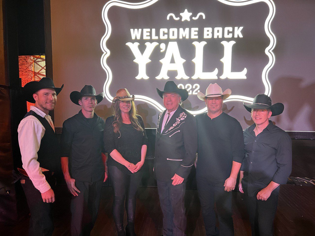 A group of people standing in front of a welcome back y ' all sign.